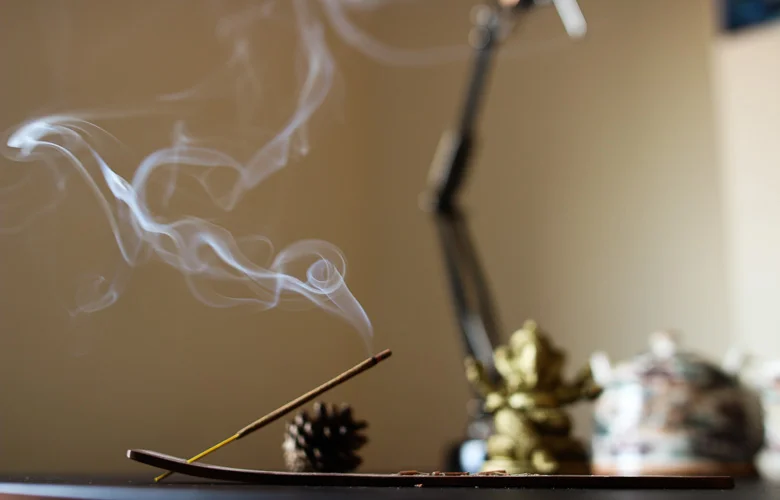 Incenso aceso liberando fumaça branca, criando uma atmosfera de purificação e proteção espiritual. Incenso natural em suporte decorativo, ideal para rituais de limpeza energética e meditação